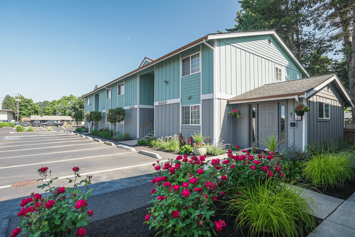 Charming residential apartment building with vibrant landscaping and ample parking, set against a clear blue sky.