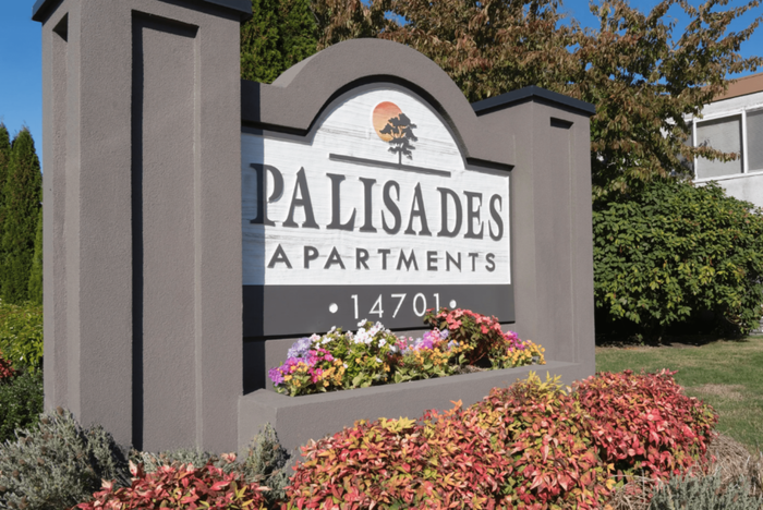 Elegant entrance sign for Palisades Apartments surrounded by lush greenery and vibrant flowers, highlighting welcoming and tranquil living spaces.