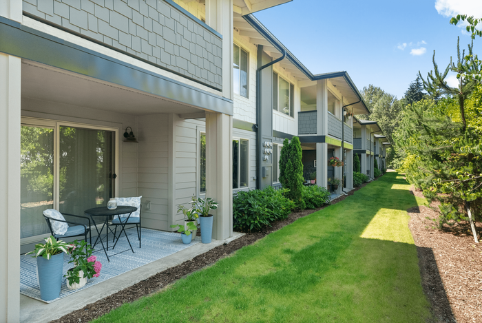 Charming apartment exterior with private patio, lush greenery, and inviting outdoor seating.
