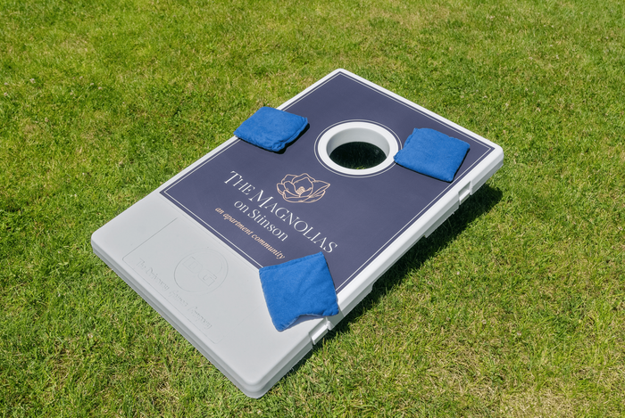 Inviting lawn game setup with branded cornhole board at The Magnolias on Stinson, perfect for resident leisure.