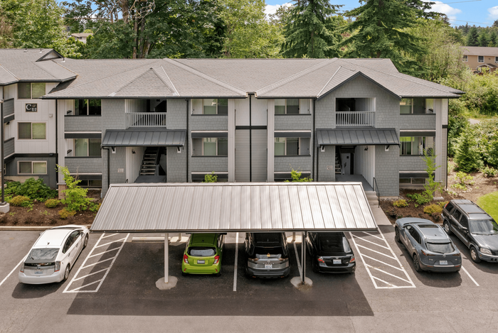 Modern apartment complex with a charming gray exterior, surrounded by lush greenery and featuring a convenient covered parking area.