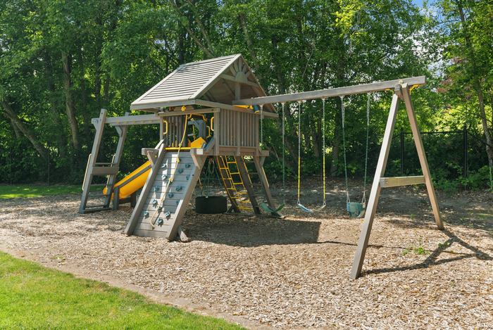 Charming outdoor playset surrounded by lush greenery, featuring a climbing wall, swings, and a slide for endless fun.