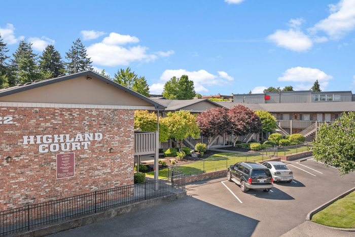 Charming Highland Court apartment complex with lush greenery and ample parking under a bright blue sky.