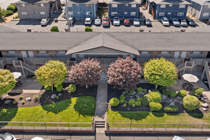 Charming apartment complex with beautiful landscaping, mature trees, and inviting outdoor seating areas.