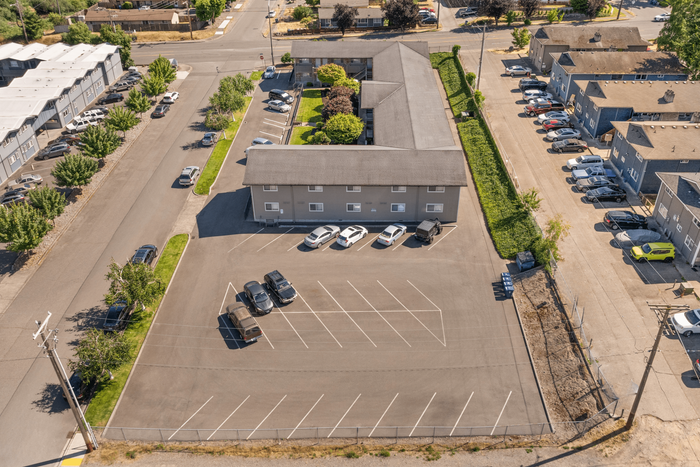 Aerial view of a modern apartment complex featuring ample parking spaces, lush greenery, and well-maintained surroundings.