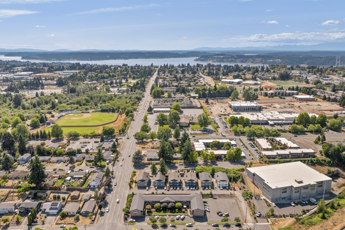 Stunning aerial view of a vibrant community with lush greenery, a baseball field, and a sprawling neighborhood against the backdrop of serene water and mountains.