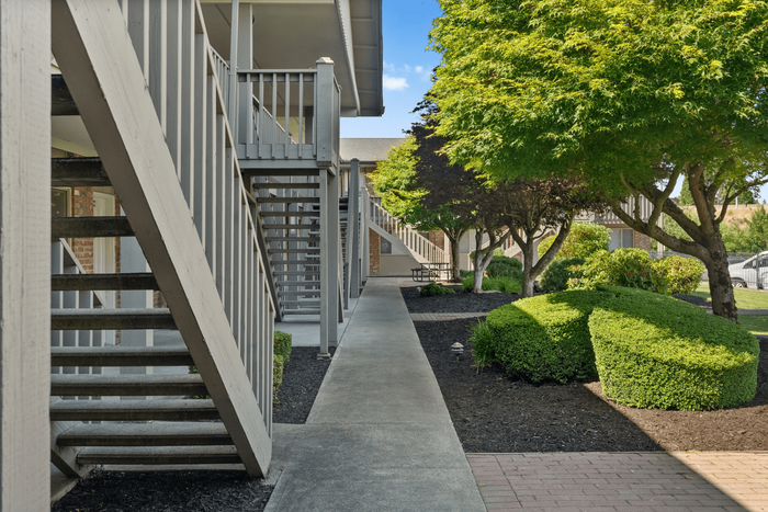 Charming apartment exterior with inviting wood stairs and lush green landscaping, perfect for a serene living experience.