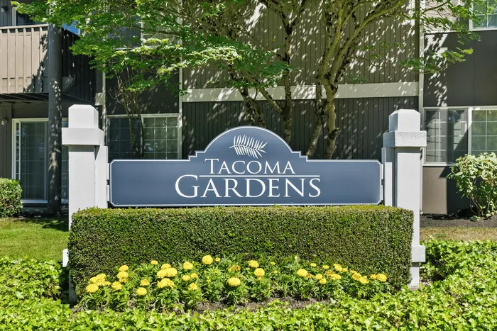 Charming Tacoma Gardens entrance sign surrounded by lush greenery and vibrant yellow flowers, offering a welcoming and serene community ambiance.