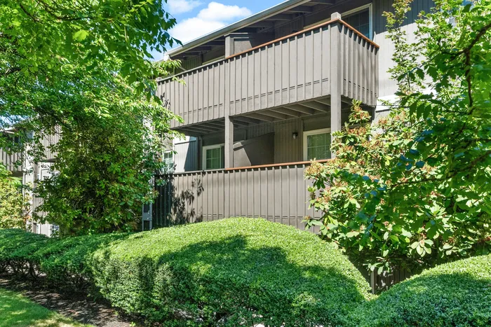 Charming apartment exterior with private balcony, surrounded by lush greenery and vibrant shrubbery.
