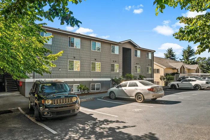 Charming apartment building with ample parking and lush greenery on a bright sunny day.