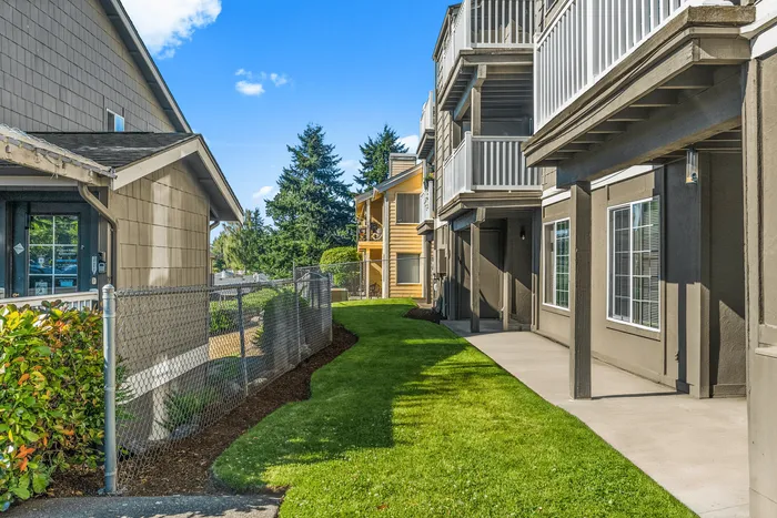 Charming apartment exterior featuring lush green landscaping and inviting balconies under a clear blue sky.
