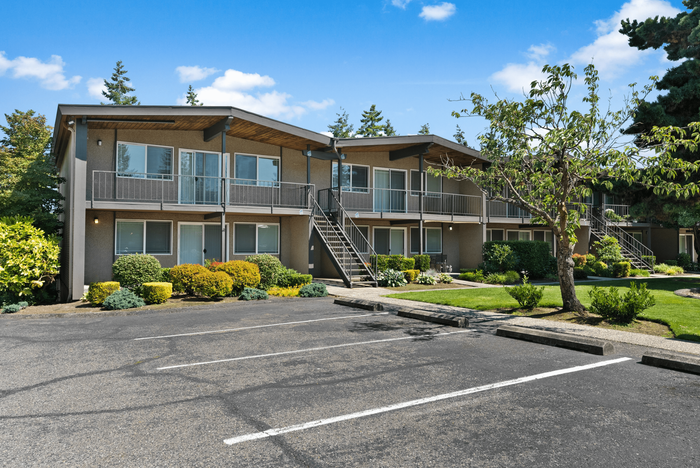 Charming apartment complex featuring landscaped gardens, private balconies, and ample parking under a clear blue sky.