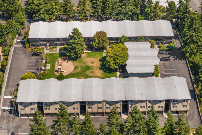 Charming aerial view of a cozy apartment complex with beautifully landscaped central courtyard and ample parking.
