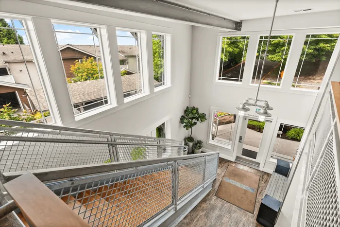 Bright, modern stairwell with expansive windows and scenic outdoor views, featuring sleek metal railing and lush indoor plants.