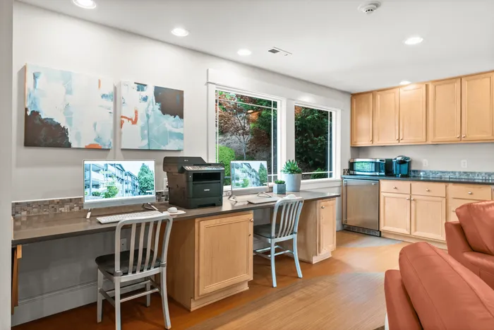 Bright and modern home office space with dual workstations, stylish wood cabinetry, and large window offering a scenic garden view.