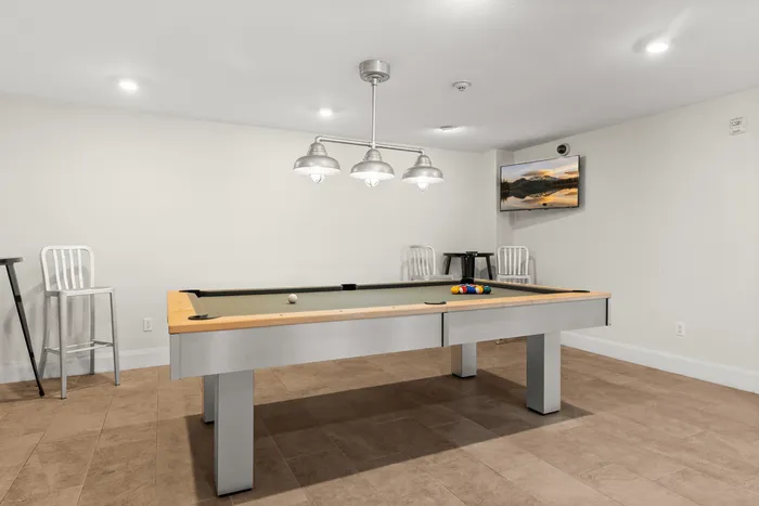 Inviting recreation room with a sleek pool table under stylish modern lighting, perfect for entertainment and relaxation.