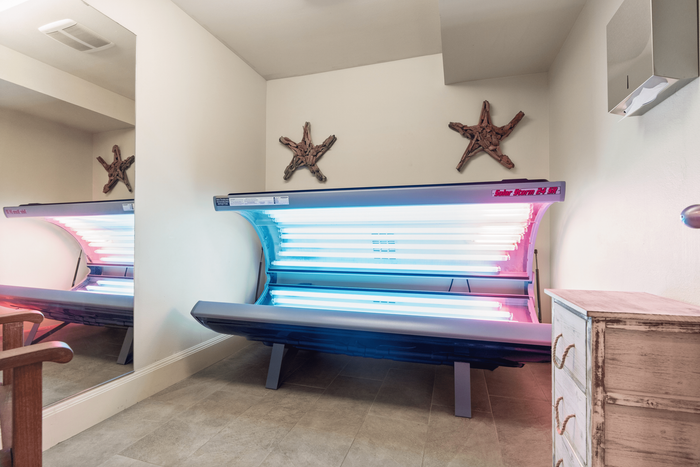 Bright and inviting tanning room featuring a sleek, state-of-the-art sunbed. The space is warmly decorated with starfish wall accents and offers a modern, serene atmosphere.