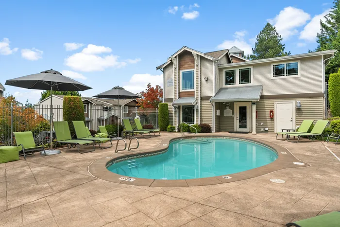 Inviting outdoor pool area with stylish lounge chairs and umbrellas, nestled beside a modern townhome.