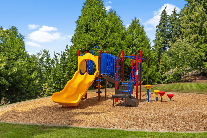 Vibrant playground with a yellow slide, climbing structures, and surrounded by lush greenery, offering a perfect family-friendly environment.