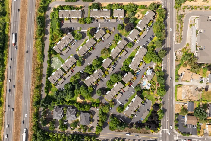 Inviting aerial view of a lush apartment complex with modern buildings, tree-lined pathways, and ample parking, conveniently located near major highways.