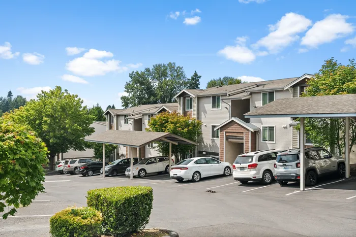 Charming apartment complex with modern architecture, ample parking, and lush greenery under a clear blue sky.