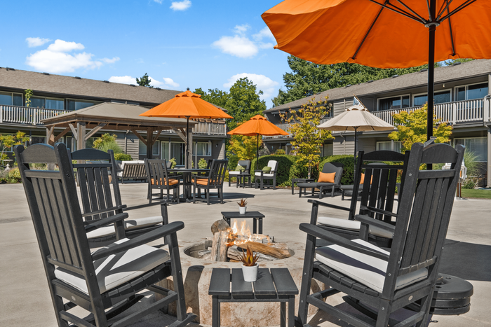 Inviting courtyard with cozy seating around a fire pit, enhanced by vibrant orange umbrellas and lush greenery, ideal for relaxation and social gatherings.