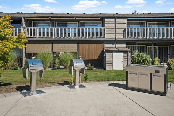 Inviting outdoor community area featuring stainless steel grills and lush landscaping, perfect for social gatherings.