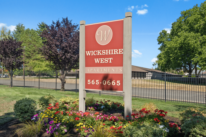 Charming Wickshire West Apartments sign set against a backdrop of lush greenery and vibrant flowerbeds, offering an inviting and picturesque living environment.
