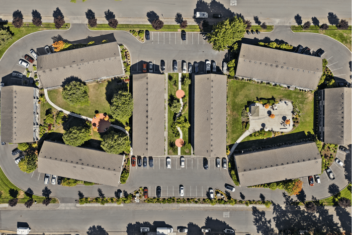 Aerial view of a charming apartment complex featuring beautifully landscaped gardens, multiple inviting outdoor spaces, and convenient parking areas.