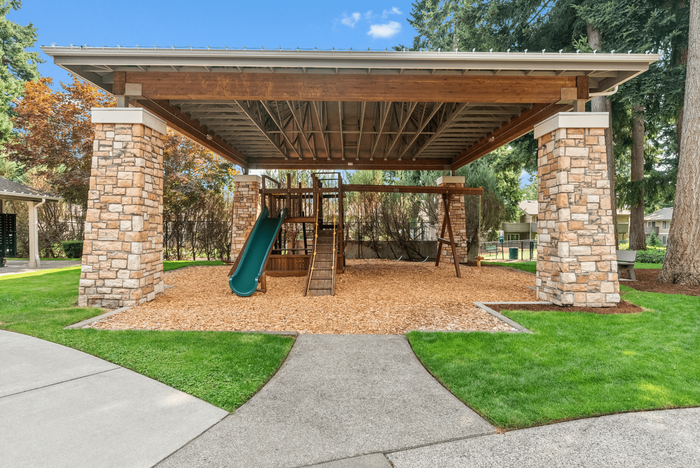 Charming outdoor playground with a slide and swings under a stylish pergola in a lush green park setting.