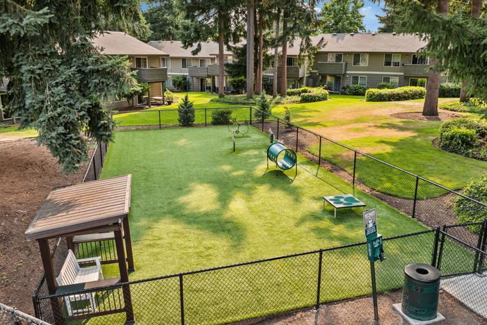 Charming apartment community featuring a lush fenced dog park with agility equipment and cozy seating area, surrounded by well-maintained landscaping and welcoming homes.