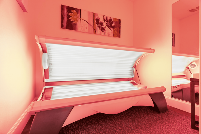 Modern tanning bed in a chic, warmly-lit room with stylish floral artwork and a large mirror.