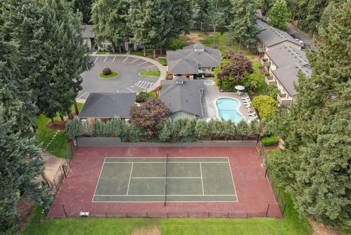 Aerial view of a serene residential complex with lush greenery, inviting swimming pool, and a spacious tennis court, offering luxurious amenities and tranquil living.