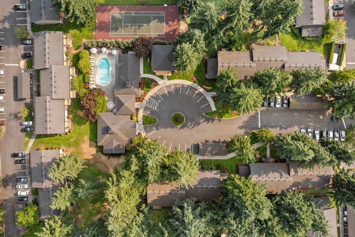 Aerial view of a vibrant apartment complex featuring a central circular driveway, pristine swimming pool, tennis courts, lush greenery, and ample parking.