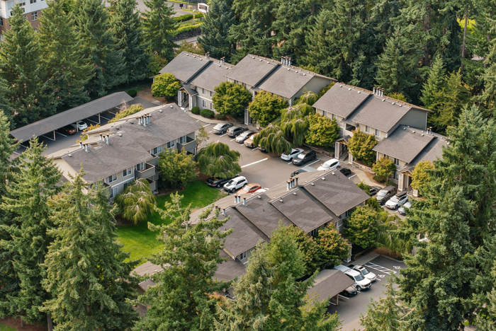 Charming aerial view of a lush, tree-lined apartment community featuring adjacent parking and inviting outdoor spaces.