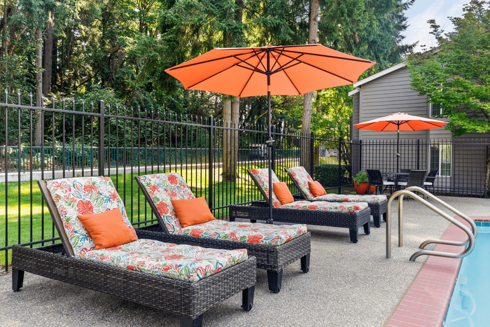 Charming outdoor oasis with wicker lounge chairs, vibrant floral cushions, and orange parasols beside a sparkling pool amidst lush greenery.