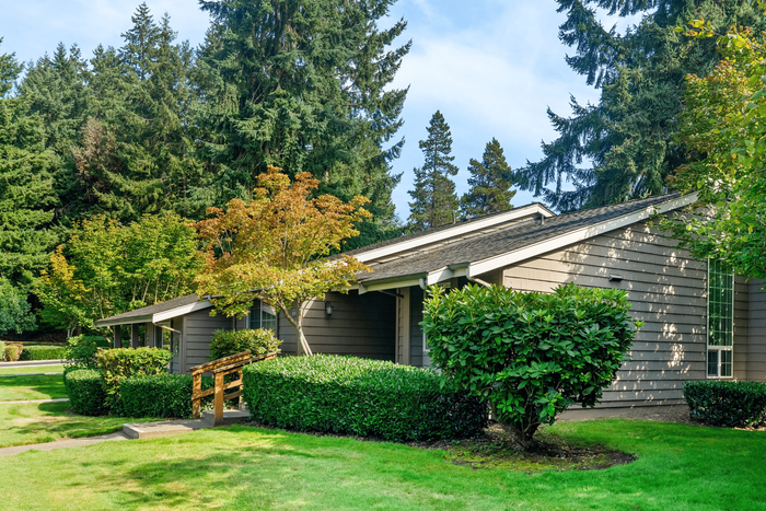 Charming single-story home with lush greenery, manicured lawns, and a serene woodland backdrop.