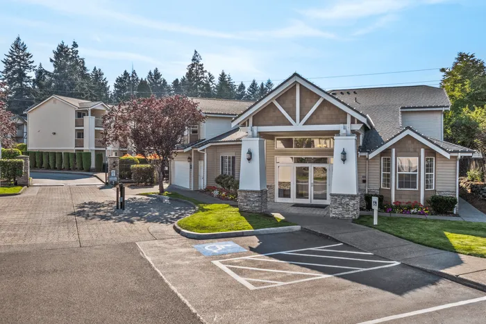 Inviting apartment complex entrance with manicured lawns, vibrant flower beds, and modern architectural design against a backdrop of lush trees.