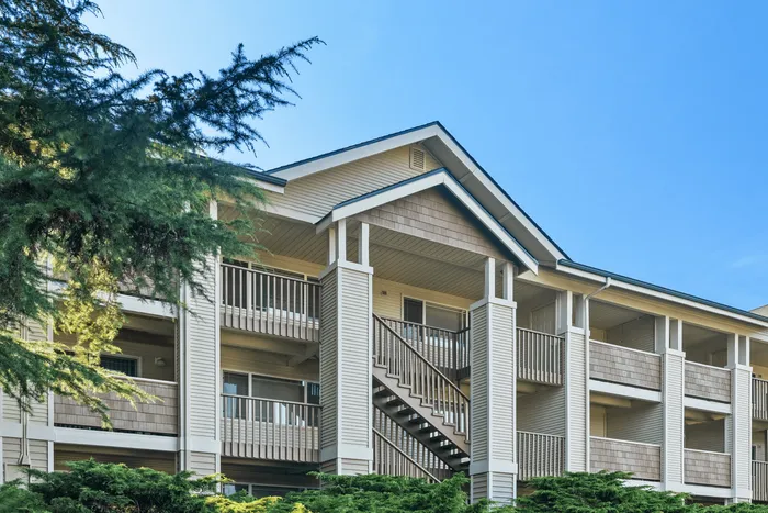 Charming multi-level apartment building with spacious balconies and lush greenery under a clear blue sky.