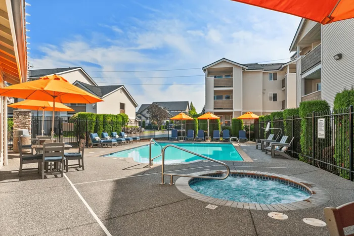 Inviting outdoor pool area with bright orange umbrellas, comfortable lounge chairs, and a bubbling hot tub, perfect for relaxation and enjoyment.