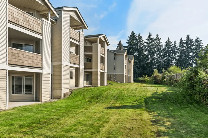 Charming apartment complex with spacious balconies, lush green lawns, and a serene natural backdrop.