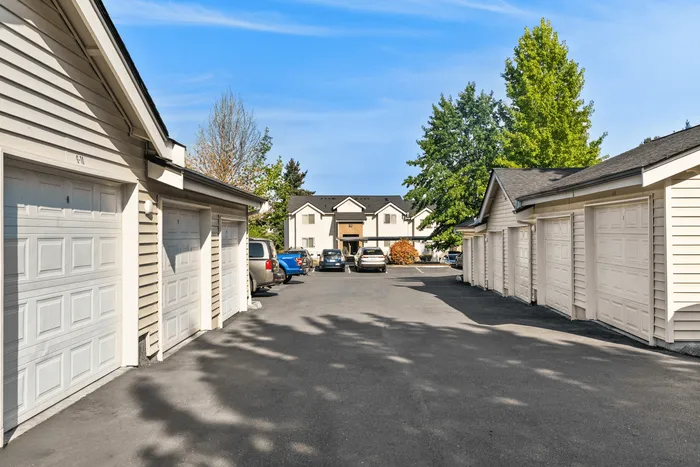 Inviting residential parking area lined with individual garages, set against a backdrop of lush greenery and a charming apartment building.