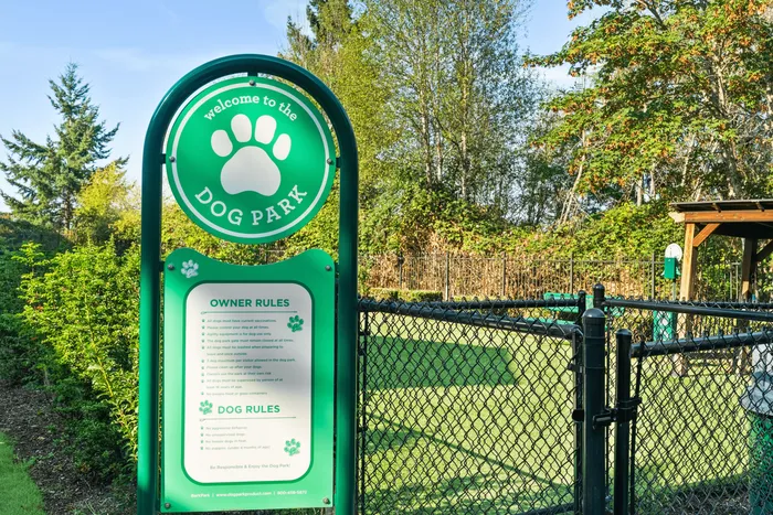 Inviting dog park entry sign with clear rules, surrounded by lush greenery and fenced play area.