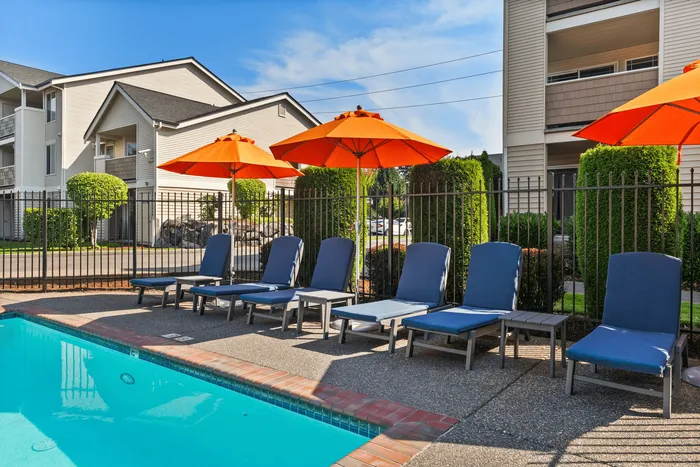 Inviting outdoor pool area with stylish sun loungers under vibrant orange umbrellas, perfect for relaxation and leisure.
