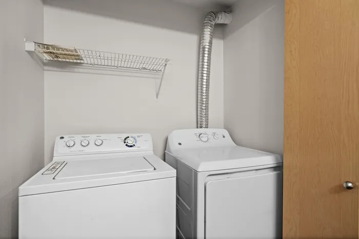 Compact laundry area with modern white washer and dryer, featuring convenient overhead shelving for storage.