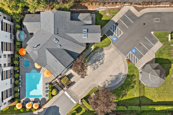Stunning aerial view of a luxury apartment complex featuring a sparkling pool, sunlit umbrellas, vibrant green spaces, and convenient parking facilities.