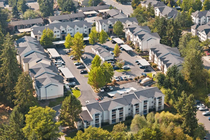 Aerial view of a picturesque apartment complex with neatly arranged buildings, lush green surroundings, and ample parking space.