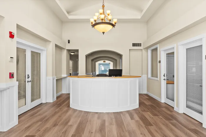 Elegant office lobby with high ceilings, modern chandelier, and wood flooring, featuring a spacious front desk and natural light.