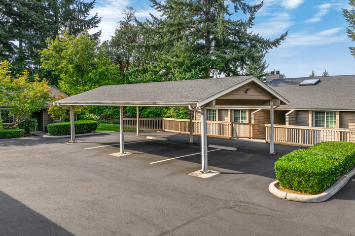 Inviting apartment exterior with covered parking, lush greenery, and a charming wood-accented design.