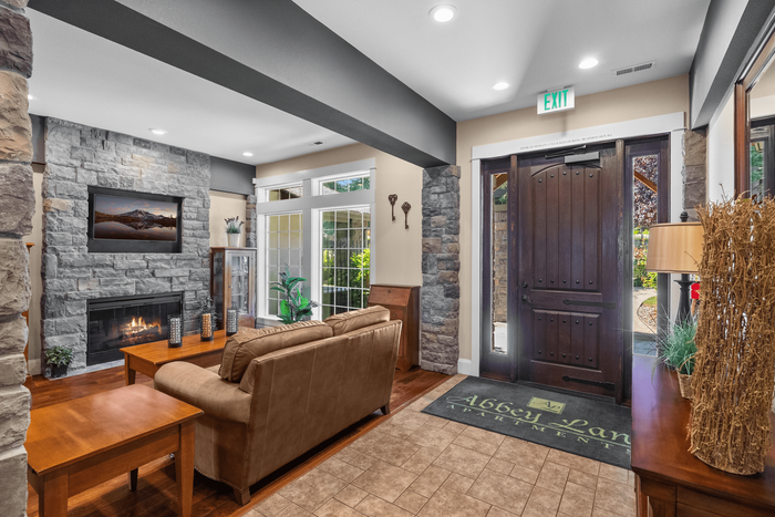 Inviting living area with stone fireplace, cozy sofa, and elegant wooden accents, offering a warm ambiance at Abbey Lane Apartments.